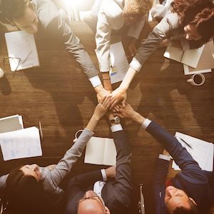 Sechs Personen strecken die Hände zusammen als Zeichen für Teamwork