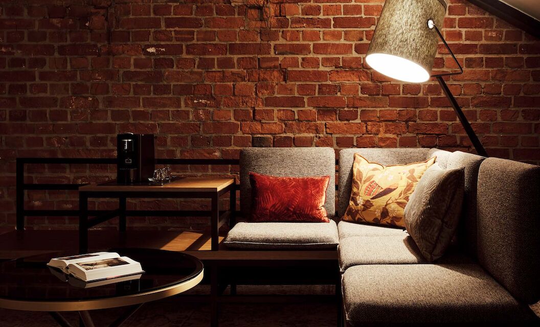 Gaswerk Hotel Hamburg Zimmer L Loft 1 L-Loft mit Sitzbereich, Stehlampe und sichtbarer Backsteinwand
