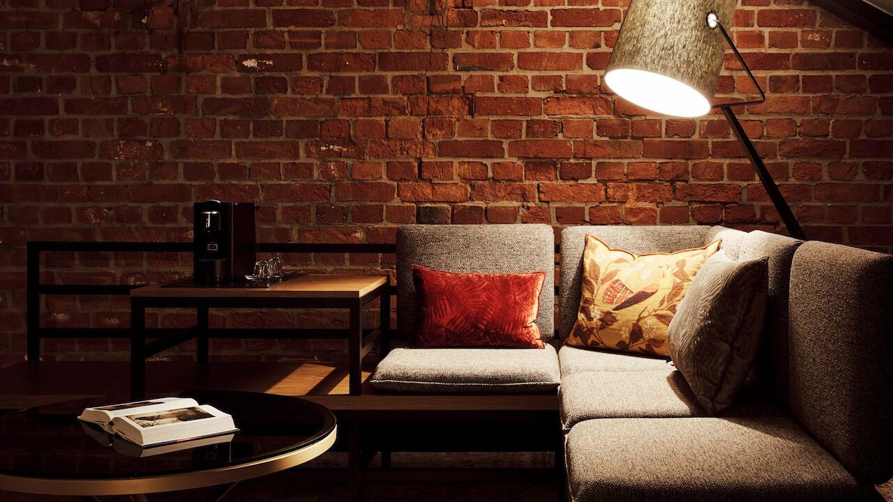 Gaswerk Hotel Hamburg Zimmer L Loft 1 L-Loft mit Sitzbereich, Stehlampe und sichtbarer Backsteinwand