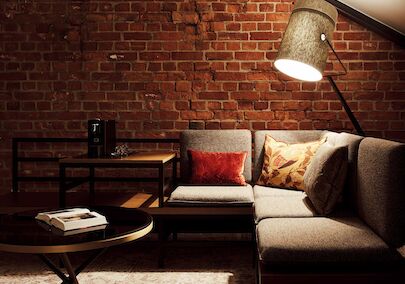 Gaswerk Hotel Hamburg Zimmer L Loft 1 L-Loft mit Sitzbereich, Stehlampe und sichtbarer Backsteinwand