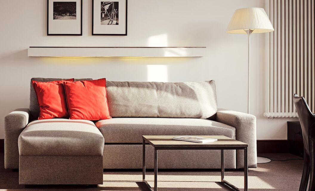 Gastwerk Hotel Hamburg Xxl Loft Zimmer 12 Graues Sofa mit Recamiere und roten Kissen, davor ein Beistelltisch