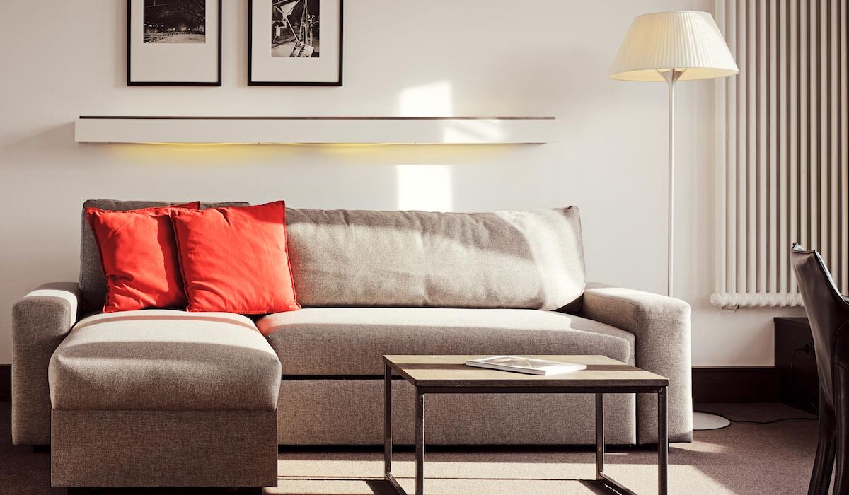 Gastwerk Hotel Hamburg Xxl Loft Zimmer 12 Graues Sofa mit Recamiere und roten Kissen, davor ein Beistelltisch