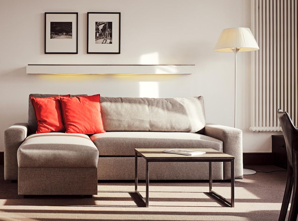 Gastwerk Hotel Hamburg Xxl Loft Zimmer 12 Graues Sofa mit Recamiere und roten Kissen, davor ein Beistelltisch