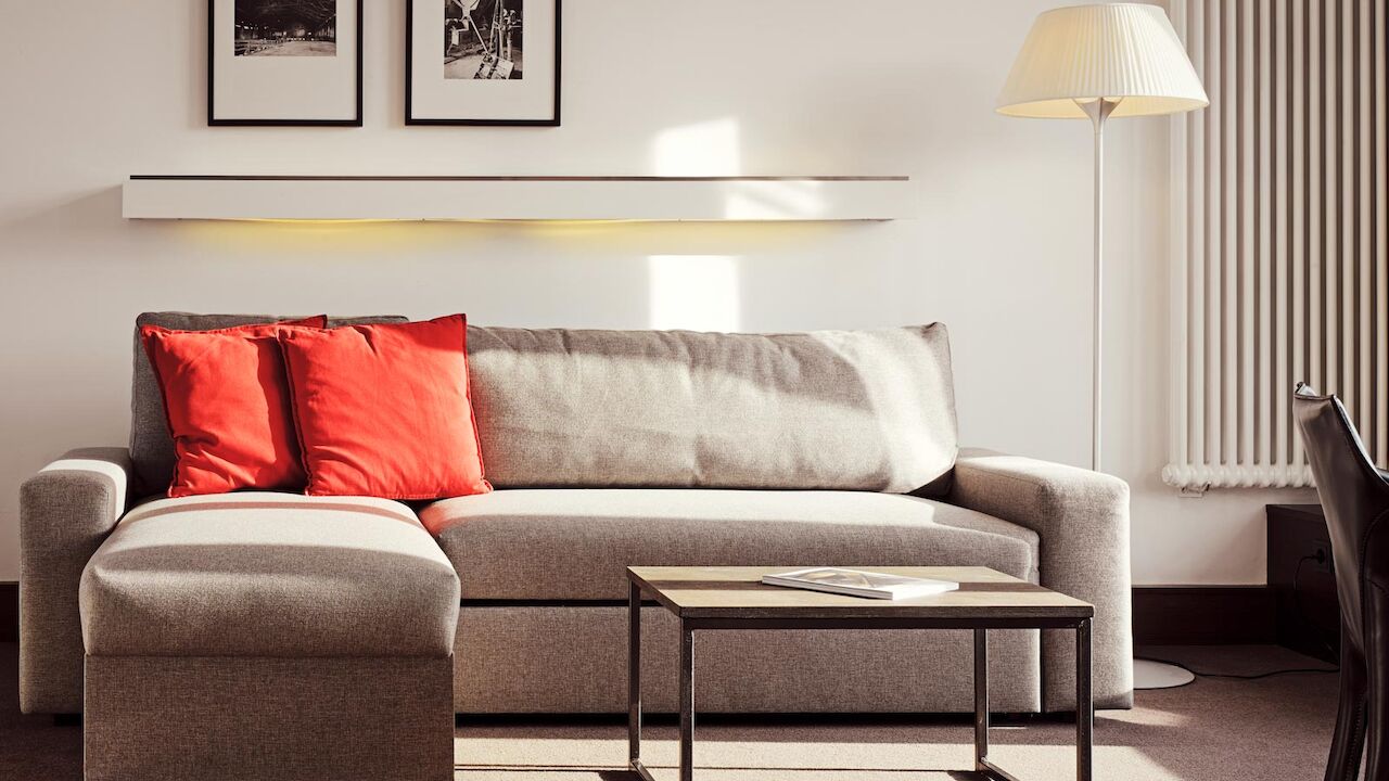 Gastwerk Hotel Hamburg Xxl Loft Zimmer 12 Graues Sofa mit Recamiere und roten Kissen, davor ein Beistelltisch