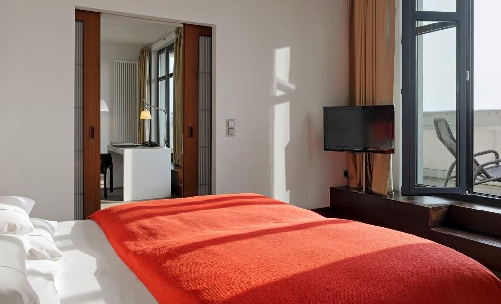 Gastwerk Hotel Hamburg Zimmer Xxl Loft 510 06 Schlafzimmer im XXL-Loft mit Bett, Fernseher und Terrasse mit Liegestühlen