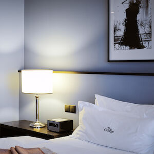 Double bed partially shown, bedside table and lamp in M-Room corner