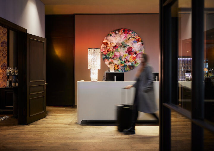 Buchwerk Hamburg Lobby 05 Frau mit Koffer passiert die Rezeption, Mitarbeiter im Hintergrund sichtbar