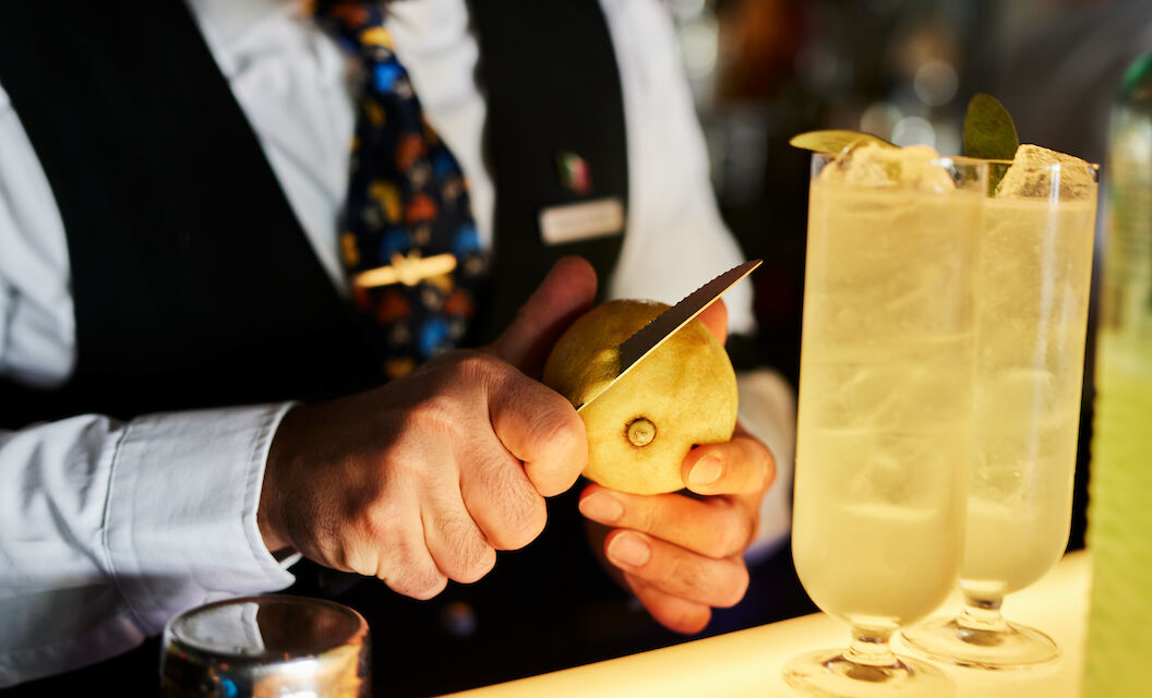 Bartender slicing lemon zest, two drinks in foreground
