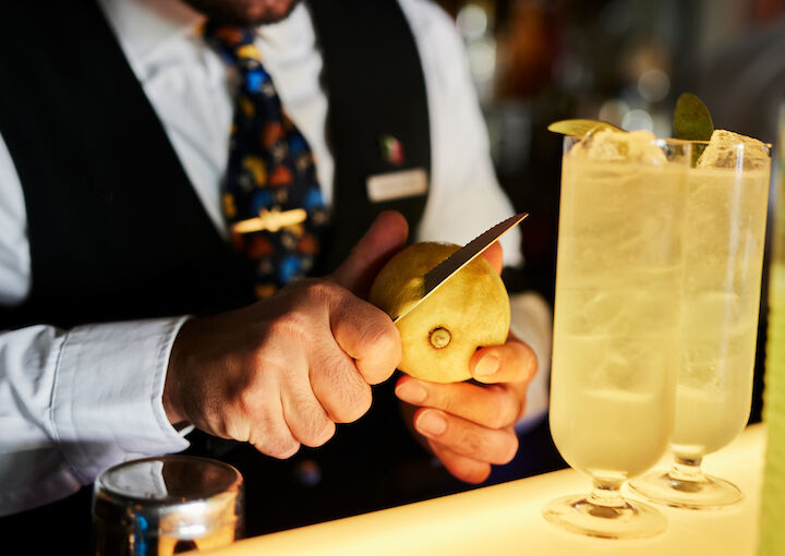 Bartender slicing lemon zest, two drinks in foreground