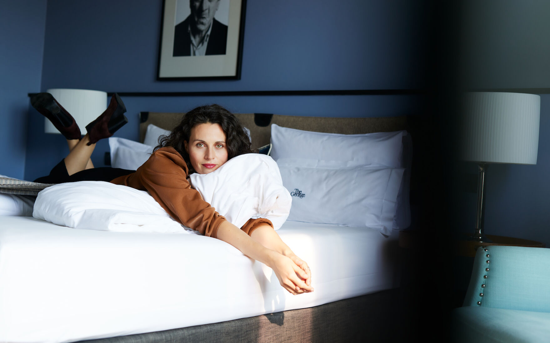 The George Hotel Hamburg Zimmer M Room People 03 Woman lying in bed in M-Room with blue wallpaper and wall art behind
