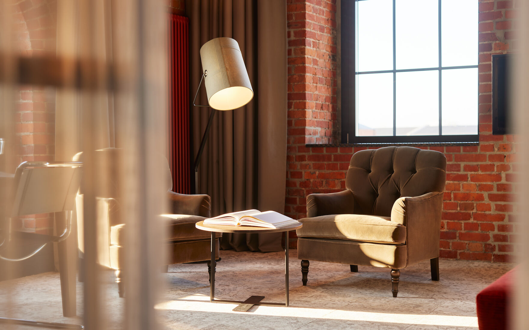 Edle Sessel, Stehlampe und Tisch mit Buch vor Backsteinwand im XL Loft