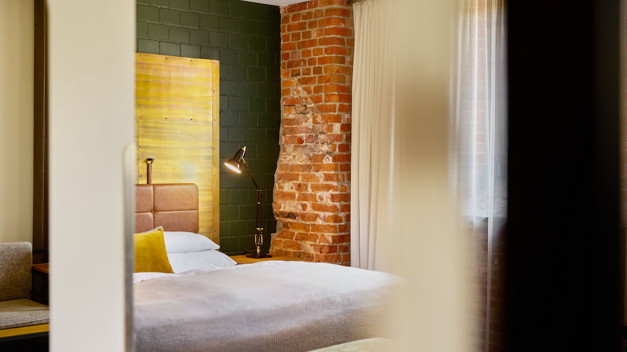 Gastwerk Hotel Hamburg Zimmer L Loft 124 01 L Loft mit großem Bett im Anschnitt und Backsteinwand im Hintergrund